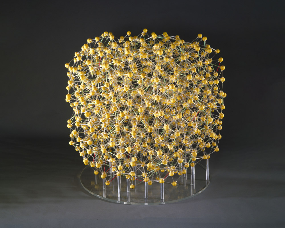 Bernal's model of the structure of a monatomic fluid, showing random close-packing. Made up of gold coloured balls with a dark grey background.