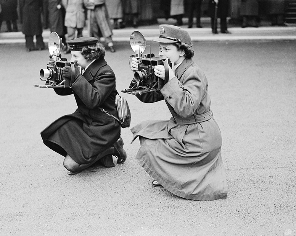 Black and white photograph of two women war photographers kneeling on ground in uniform