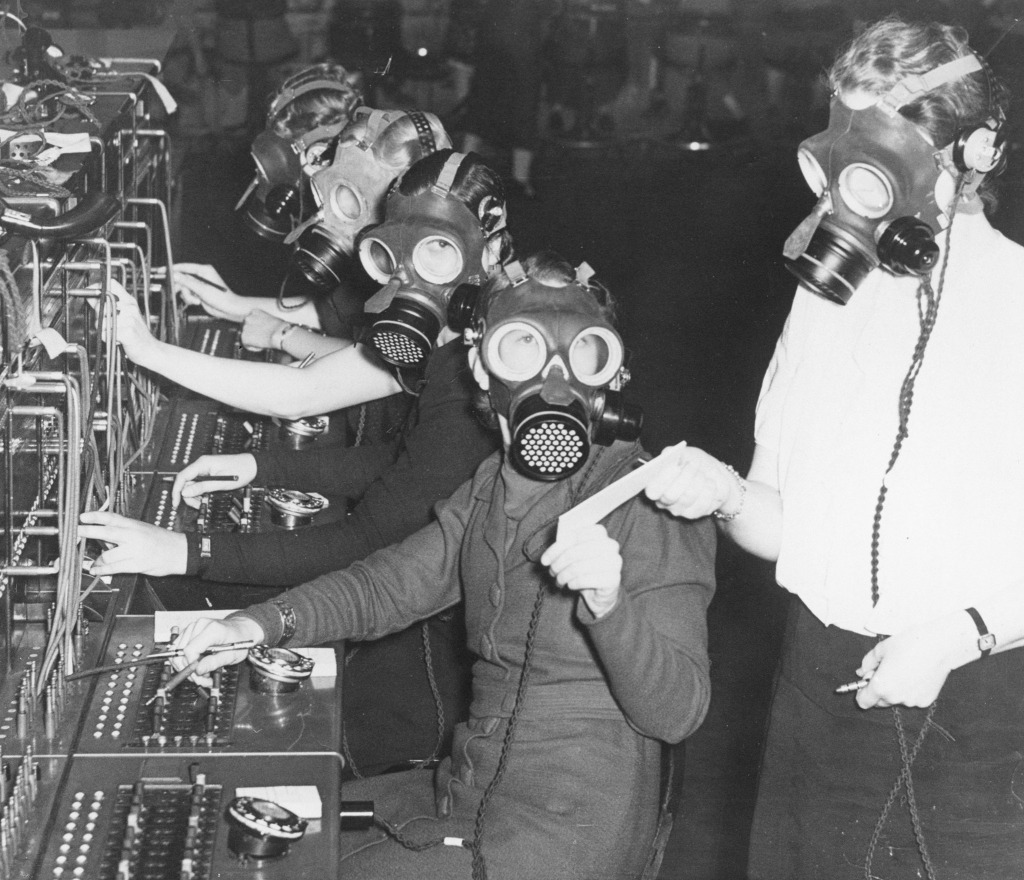 Telephone exchange operators in gas masks, 31 October 1938 Black and white photograph of telephone exchange operators in gas masks